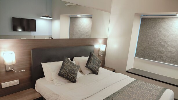 A hotel room with a bed, bedside lamps, a flat-screen TV, and a window with a view. - Apollo Guest House – Colaba Causeway (Mumbai)