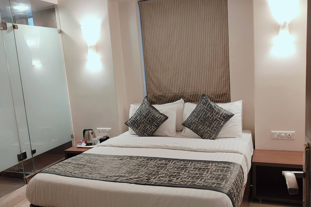 A hotel room with a bed, bedside tables, an air conditioning unit, a wardrobe, and a bathroom with a towel rack.
