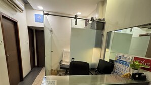 A reception desk with a glass partition, a calendar, a plant, and a no-smoking sign. - Apollo Guest House – Colaba Causeway (Mumbai)