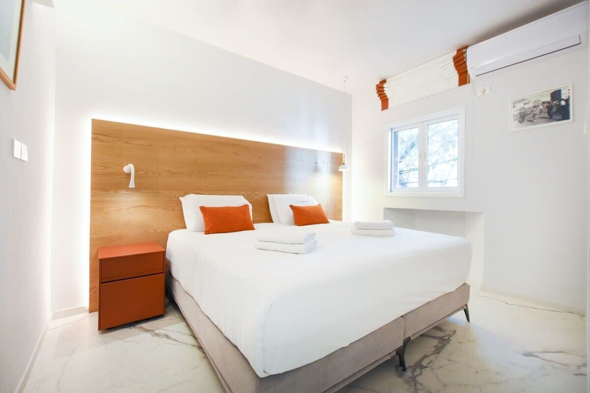 A modern bedroom with a large bed, a nightstand, a wooden headboard, and a window with a view.