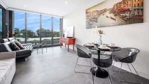 Una sala de estar moderna con un ventanal grande, una zona de comedor con una mesa de vidrio y un cuadro de una escena de canal.