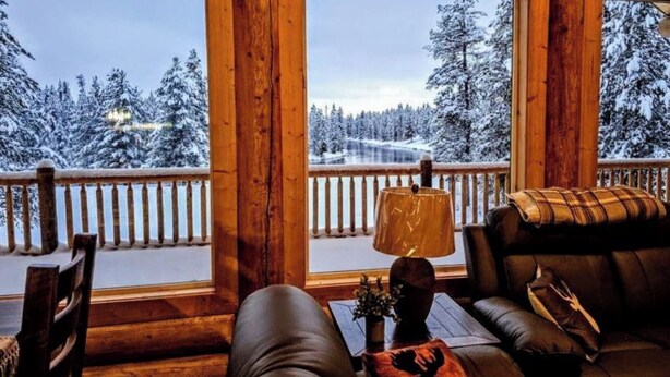 En stuga byggd av timmer med en inredning som ger utsikt över ett snötäckt landskap genom stora fönster.