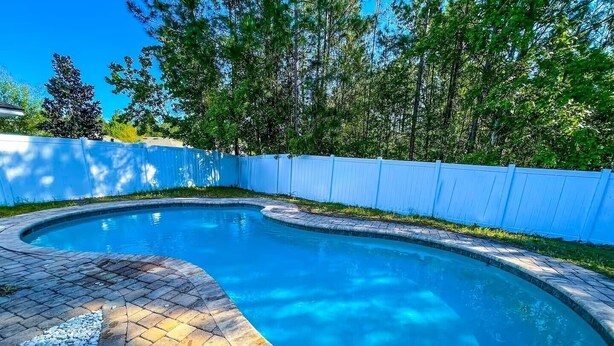 Une piscine à bord incurvé, entourée d’une clôture bleue et d’une terrasse en pierre.