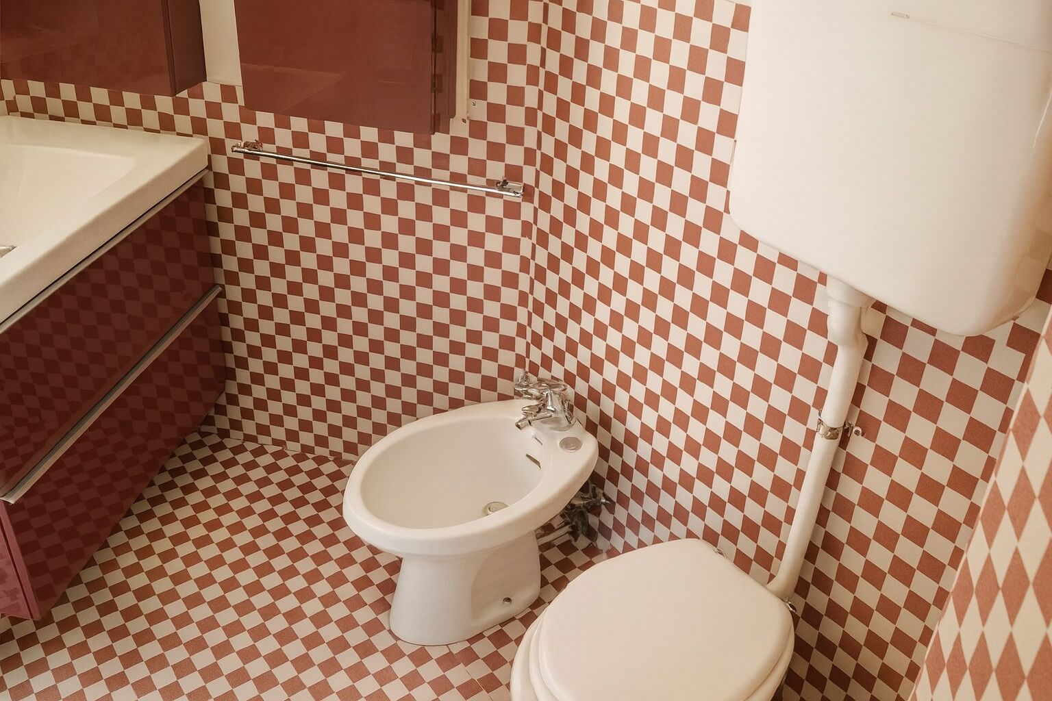 Un bagno con pavimento a scacchi, un water bianco e un bidet.