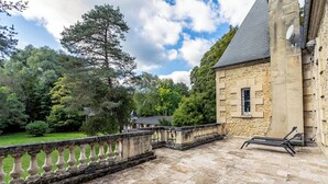 A stone building with a balcony, a lawn, and trees.