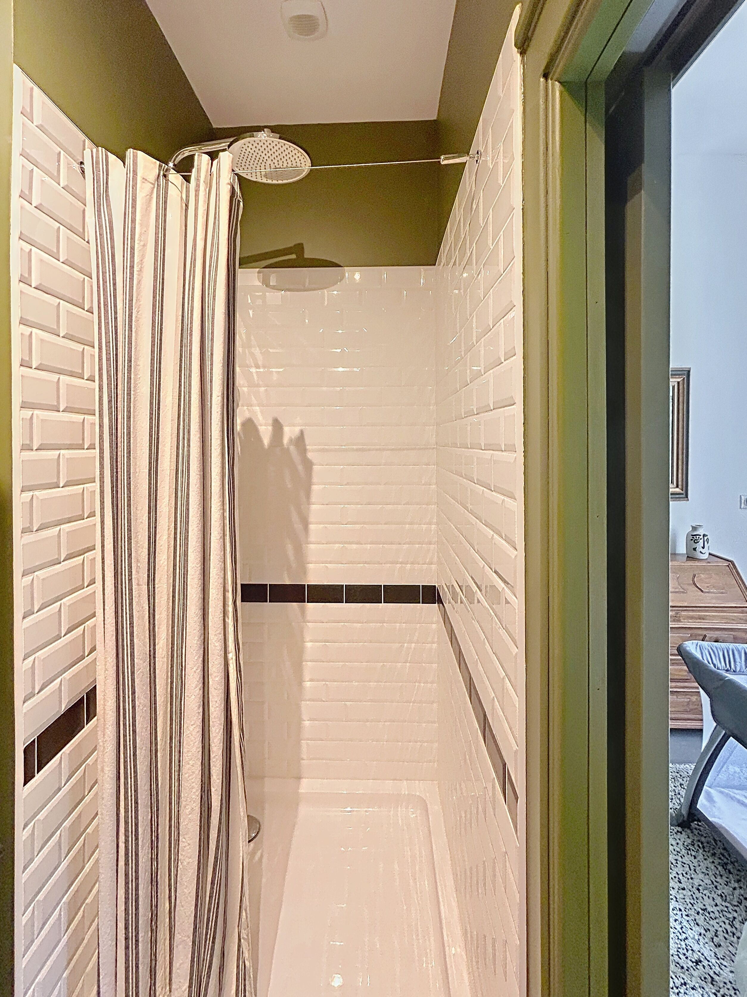 Een douche met een gestreept gordijn, witte betegelde wanden en een deur naar een buitenruimte.