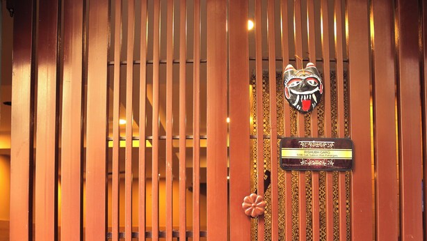 A brown metal gate with vertical slats and a decorative emblem. - Casa Central (New Delhi)