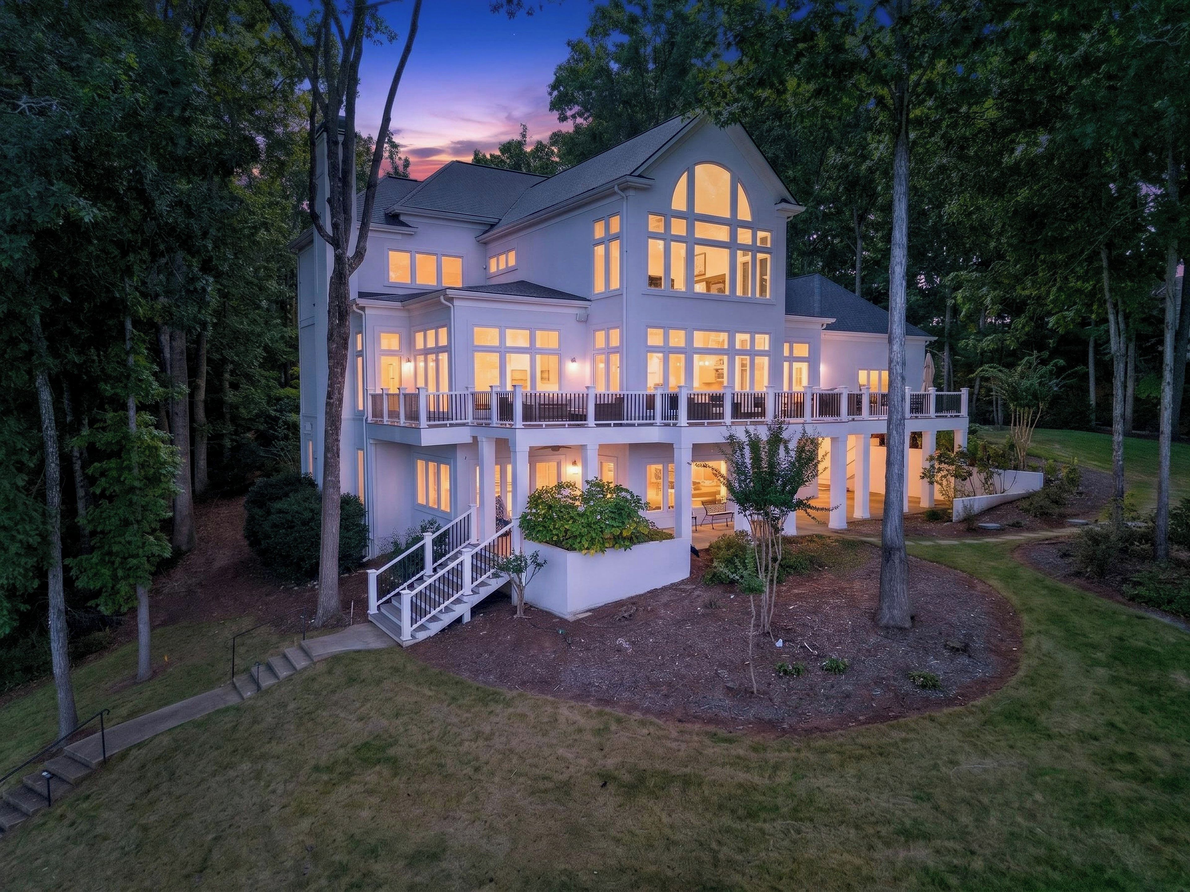 A large, multi-story house with a balcony, surrounded by trees and a well-maintained lawn.