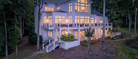 A large, multi-story house with a balcony, surrounded by trees and a well-maintained lawn.