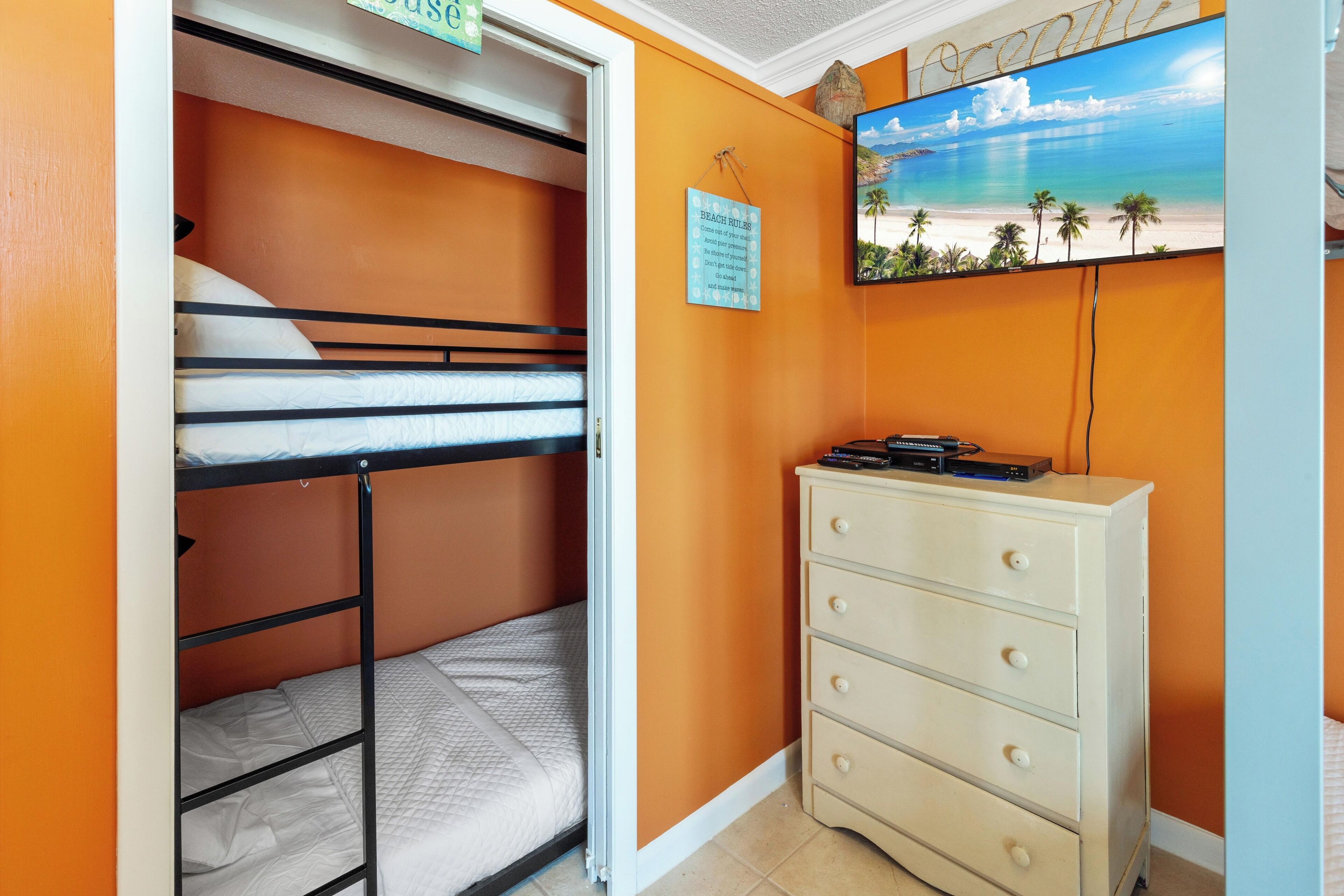 Une chambre avec un lit superposé, une commode et un tableau représentant une scène de plage.