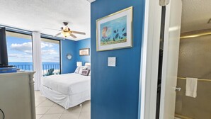 Une chambre à coucher avec un lit, une commode, un ventilateur de plafond, un tableau et une vue sur l’océan.