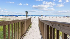 Un sentier en bois mène à une plage où l’on trouve des parasols et des personnes qui se prélassent au soleil.