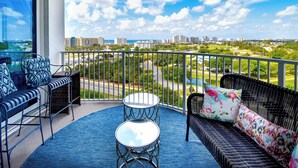 A balcony with a view of a cityscape, a wicker sofa, a small round table, and a blue rug.