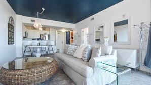 A modern living room with a sofa, glass coffee table, and a wicker ottoman.