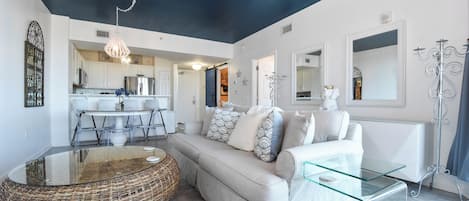 A modern living room with a sofa, glass coffee table, and a wicker ottoman.