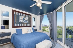 Une chambre dotée d’un grand lit, d’un ventilateur de plafond, d’un balcon avec vue sur la ville et d’une œuvre d’art moderne accrochée au mur.