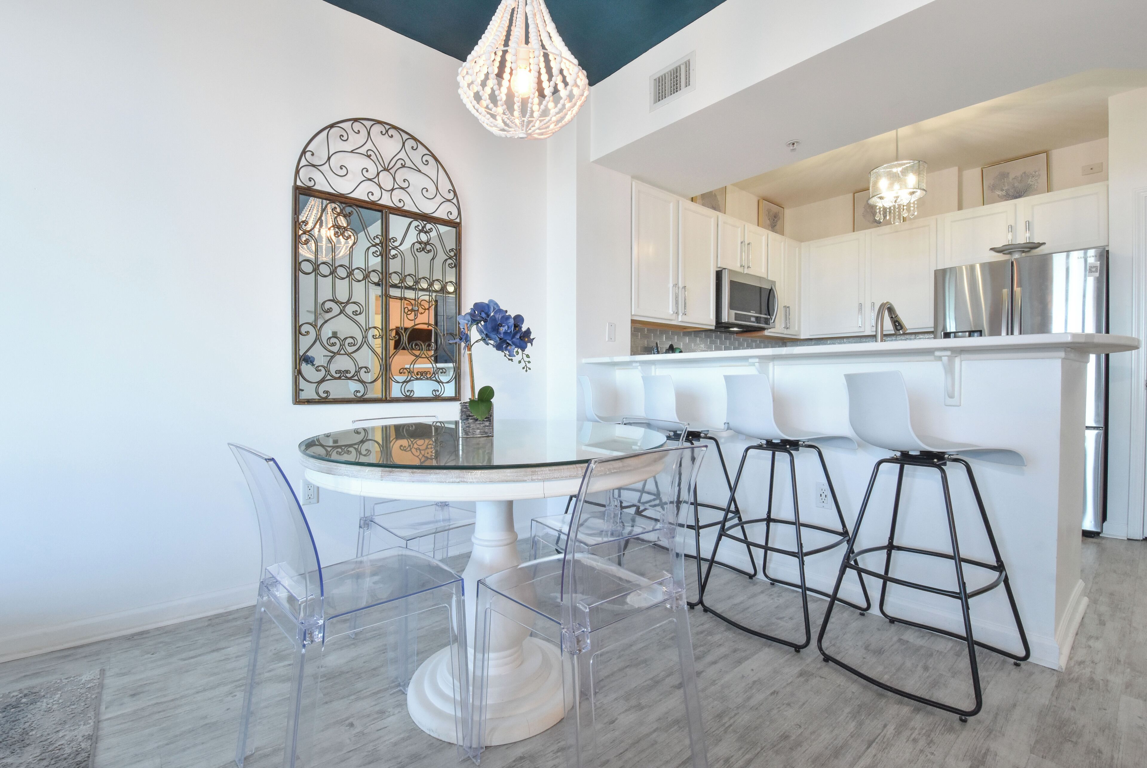 Een moderne keuken met witte kasten, roestvrijstalen apparatuur en een glazen eettafel met transparante stoelen.