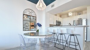 A modern kitchen with white cabinets, stainless steel appliances, and a glass dining table with clear chairs.