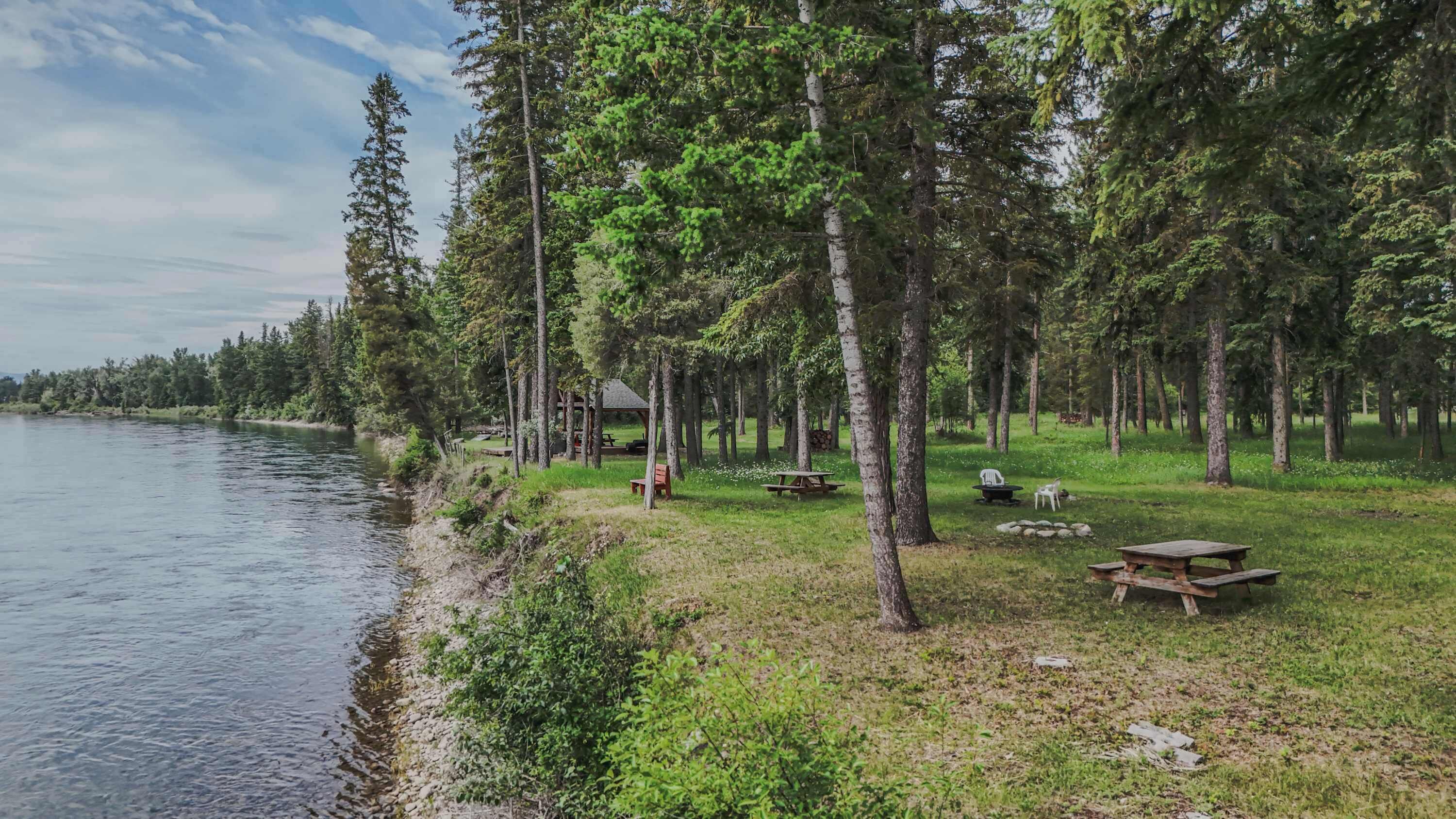 A lakeside campsite with picnic tables, a gazebo, and a small cabin.