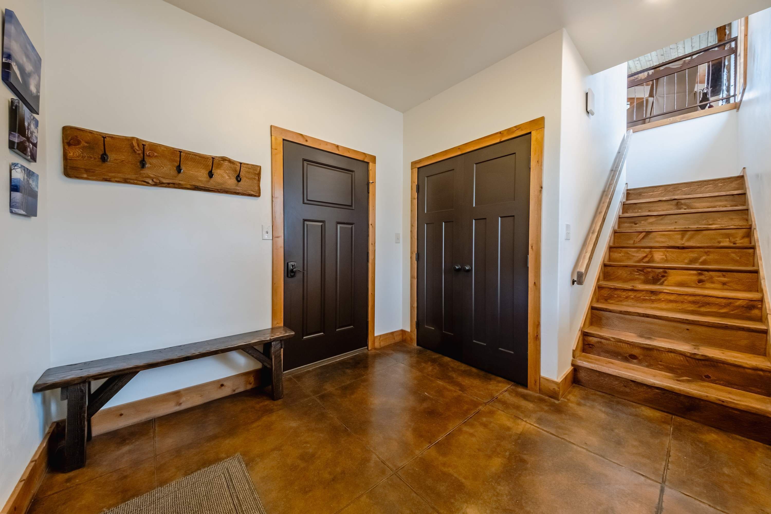 A hallway with wooden flooring, a bench, and two dark wooden doors.