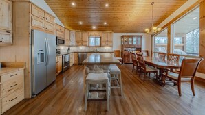 A spacious kitchen with wooden cabinets, a large island, and a dining area with wooden chairs. - Flathead River Retreat For 15! (Columbia Falls)