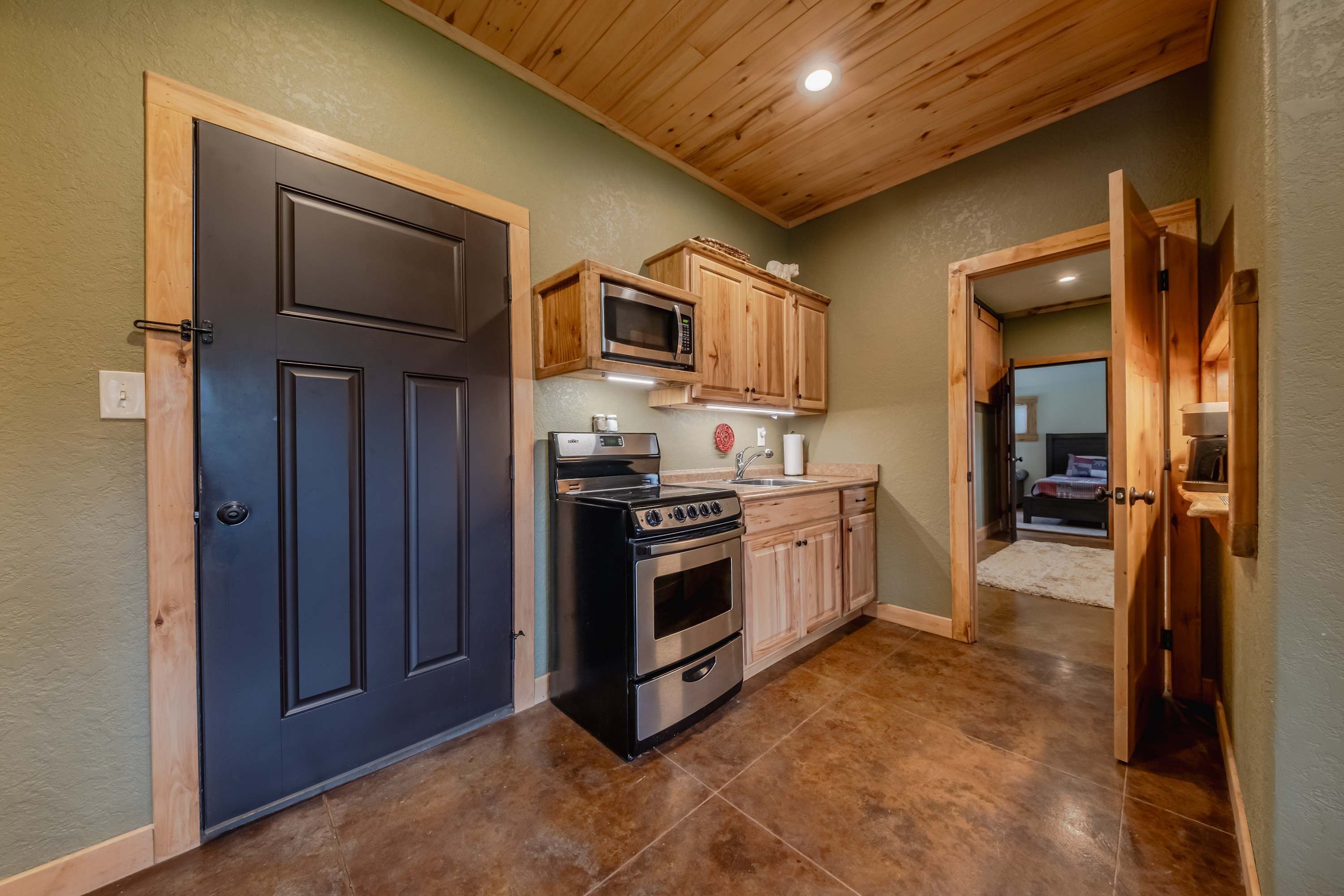 A kitchen with a black door, wooden cabinets, a microwave, a stove, and a sink.
