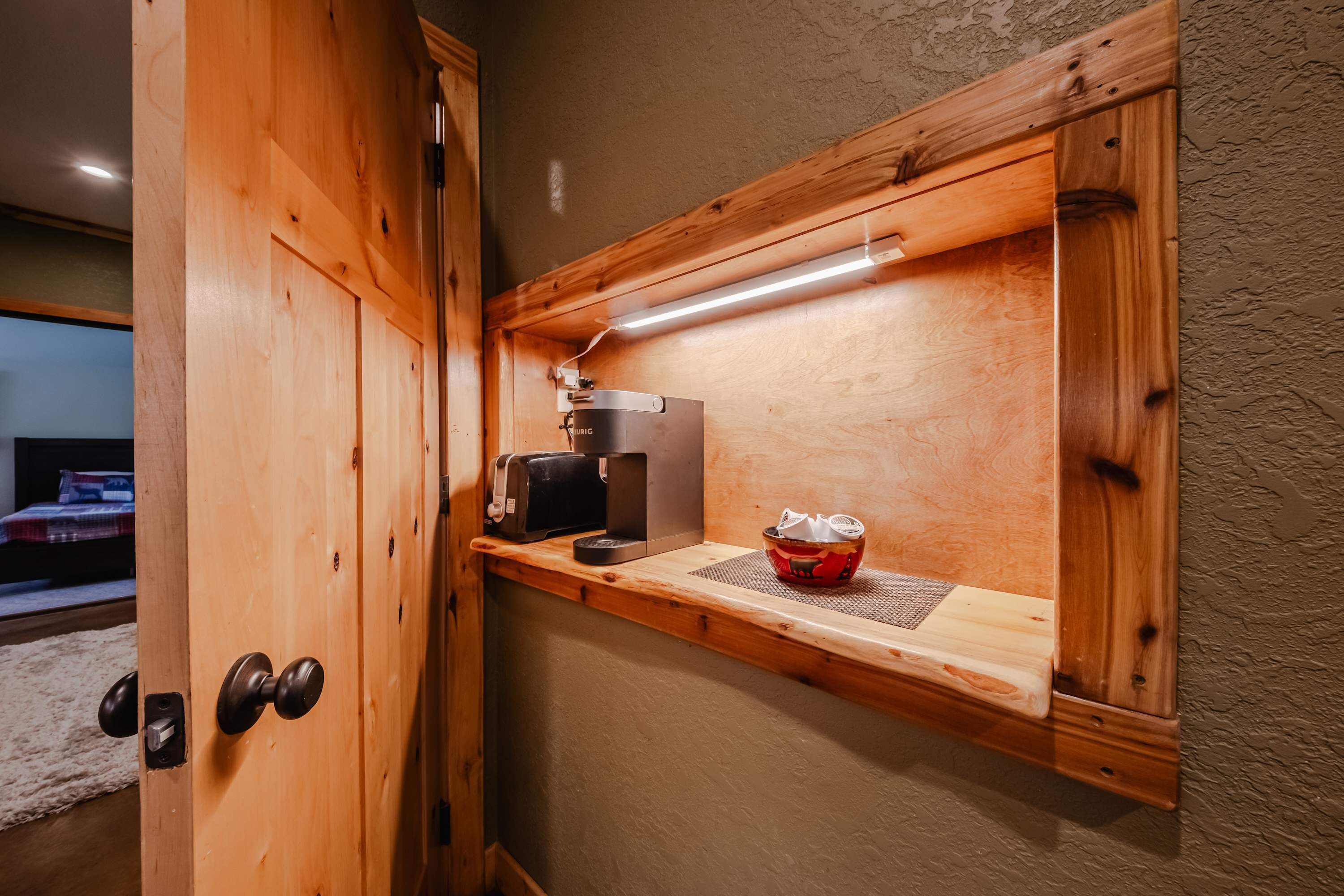 A wooden shelf with a coffee maker and a red container, a wooden door with a round handle, and a textured wall.