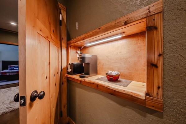 A wooden shelf with a coffee maker and a red container, a wooden door with a round handle, and a textured wall. - Flathead River Retreat For 15! (Columbia Falls)