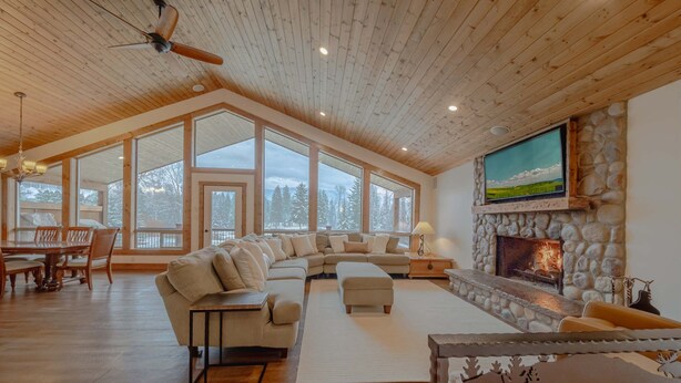 A spacious living room with a stone fireplace, large windows, and a dining area. - Flathead River Retreat For 15! (Columbia Falls)
