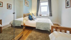 A bedroom with a bed, a bedside table, a window with curtains, and framed pictures on the wall. - Host & Stay | Hope Terrace (Amble)