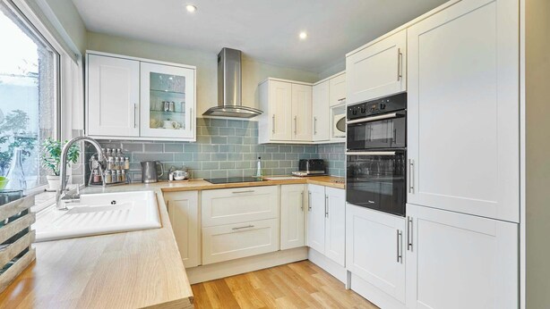 A modern kitchen with white cabinets, a stainless steel range hood, a double oven, and a wooden countertop. - Host & Stay | Hope Terrace (Amble)
