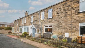 A row of stone terraced houses with a paved driveway and a small garden area. - Host & Stay | Hope Terrace (Amble)