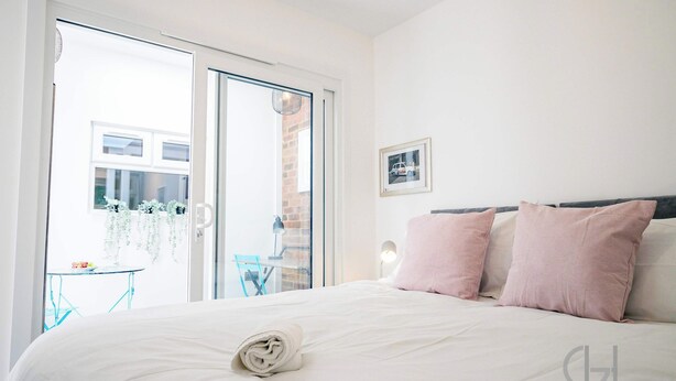A hotel room with a bed, a small table, and a chair near the window. - Host & Stay | Croydon Road Abode (Caterham)