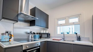 A modern kitchen with stainless steel appliances, a window with potted plants, and a built-in oven. - Host & Stay | Croydon Road Abode (Caterham)