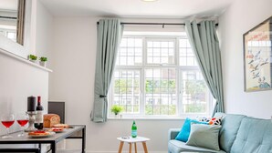 Een kamer met een raam, een tafel met eten en drinken, een bank en een klein tafeltje met een fles.