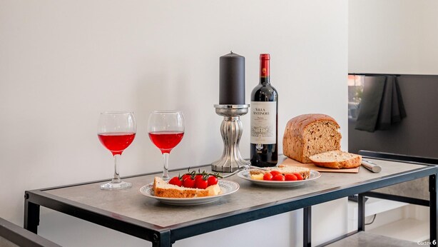 Een tafel met twee glazen rode wijn, een fles wijn, een brood en een bord met kerstomaatjes.