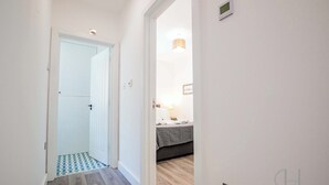 Een gang met een zwart-wit geruit vloertapijt dat leidt naar een kamer met een bed en een nachtkastje.