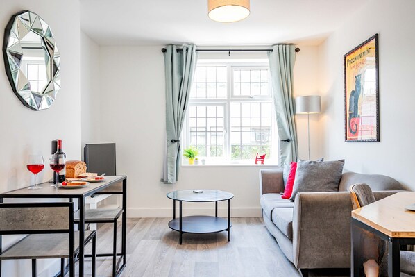 A modern living room with a dining area, a round glass table, a sofa, and a large window with curtains.