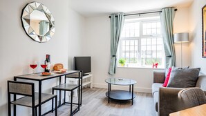 Una sala de estar moderna con comedor, una mesa redonda de vidrio, un sofá y un televisor.