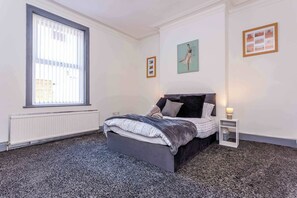 Un dormitorio con cama, ventana, radiador y un cuadro en la pared.