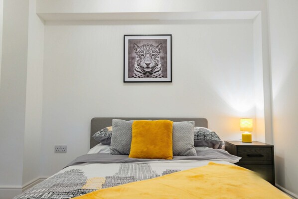 A bedroom with a bed, a nightstand, a framed picture on the wall, and a lamp.