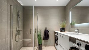 A modern bathroom with a glass-enclosed shower, a washing machine, and a sink with a mirror above it. - Penthouse with amazing fjord view (Vestland)