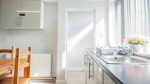 Une cuisine moderne avec une table à manger en bois, des meubles blancs et une fenêtre agrémentée de rideaux.