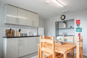 Una cocina moderna con armarios blancos, una mesa de comedor de madera y un reloj en la pared.