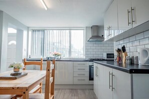 A modern kitchen with white cabinets, a black countertop, and a window with blinds.