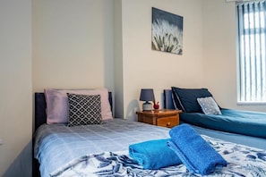 A bedroom with a bed, a nightstand, a lamp, and a window.