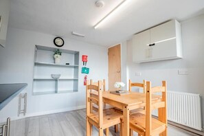 Une cuisine moderne avec une table et des chaises en bois, des meubles blancs, une horloge et une petite étagère ornée d’objets décoratifs.
