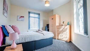 Une chambre à coucher comprenant un lit, une armoire, un bureau avec une lampe et une fenêtre avec des stores.
