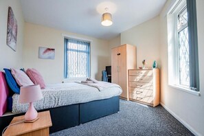 A bedroom with a bed, a wardrobe, a desk with a lamp, and a window with blinds. - Host & Stay | Park Cliffe House (Bradford)