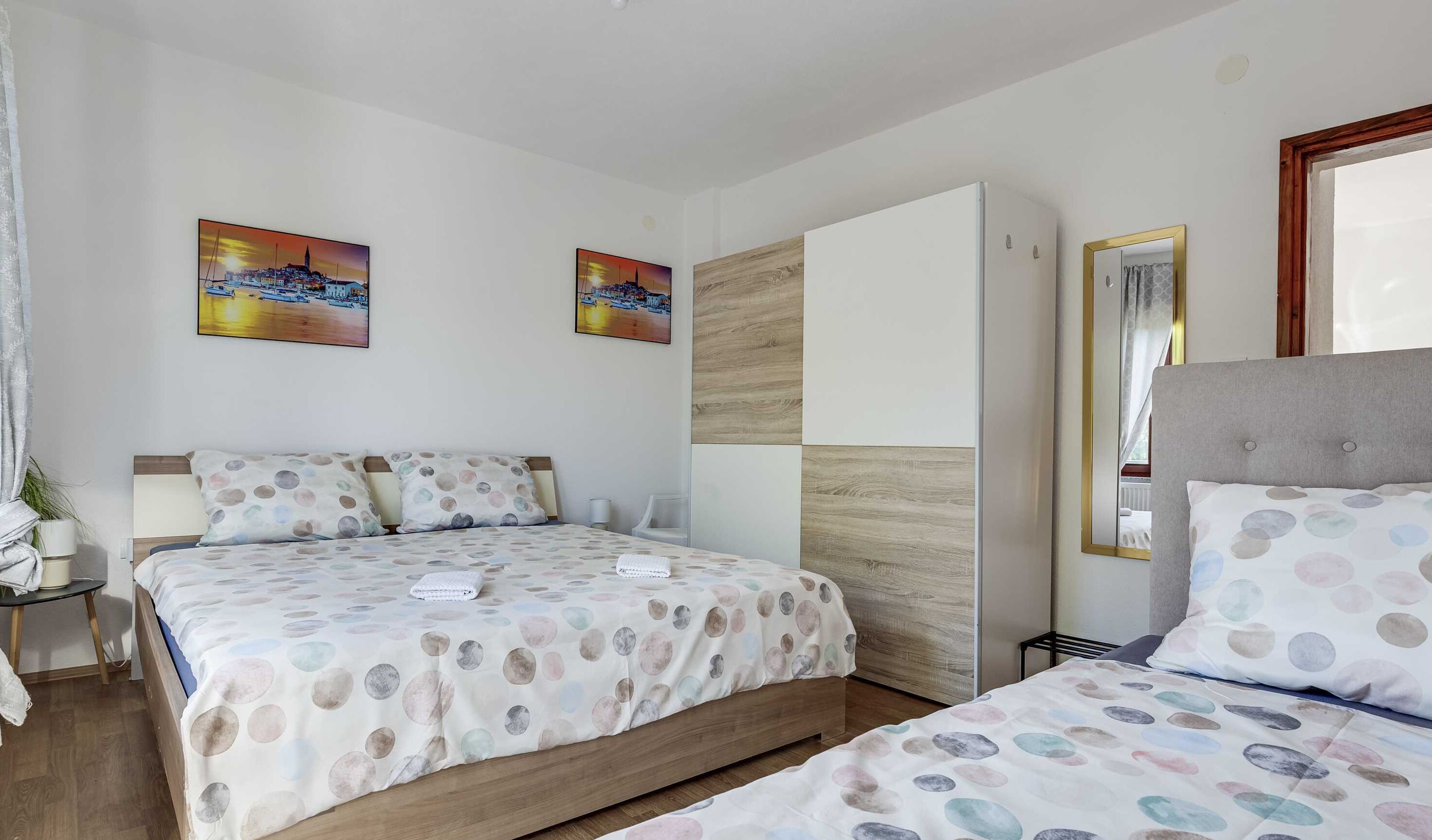Habitación de hotel con dos camas, un armario, un espejo y dos cuadros en la pared.